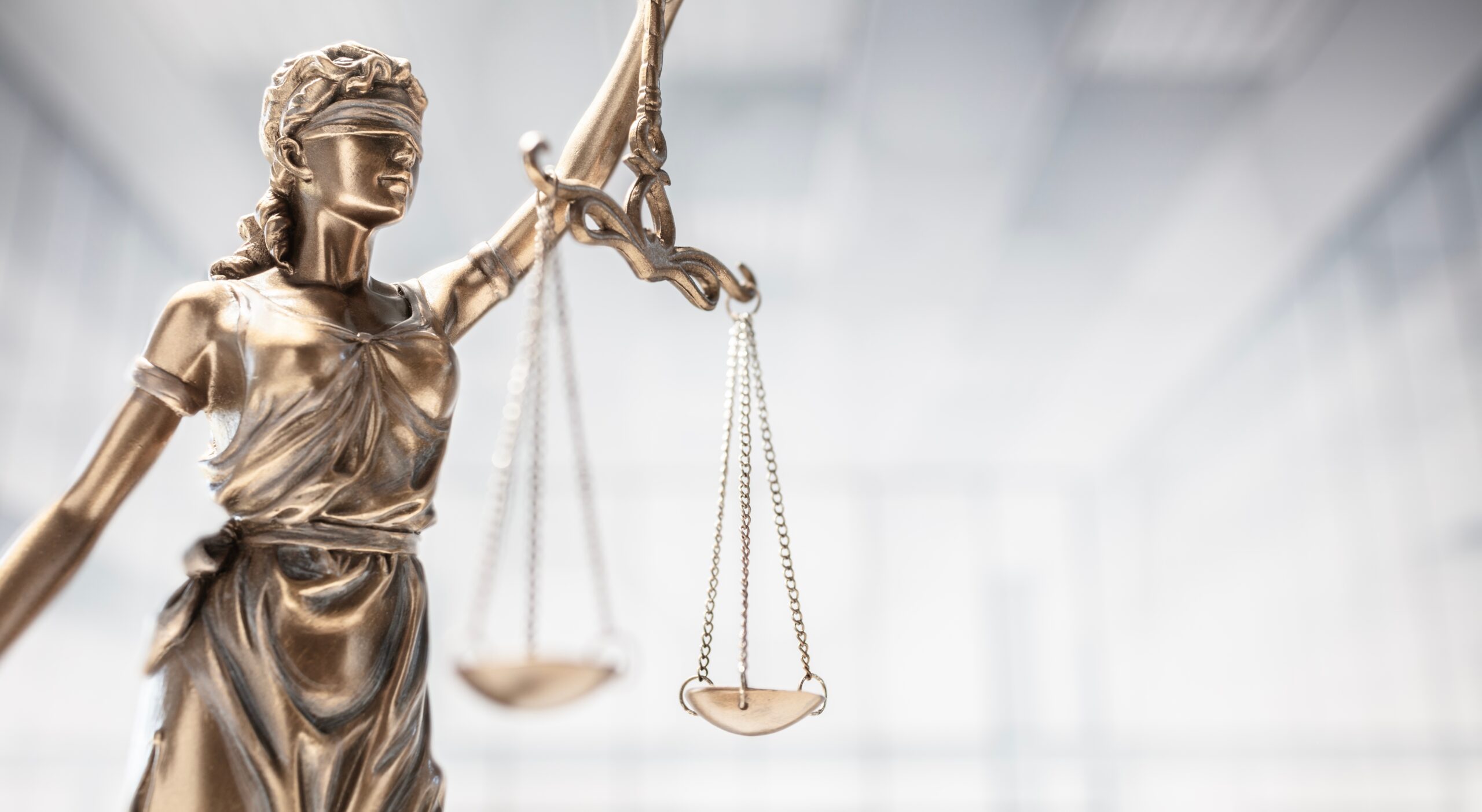 Bronze Lady Justice statue blindfolded holding balanced scales against a blurred courtroom background