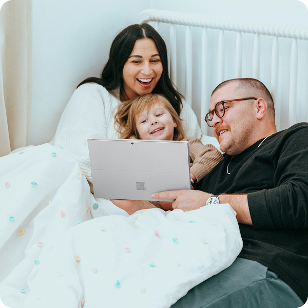 Smiling parents and young child on bed looking at a tablet