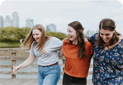 Three smiling young women walking arm‑in‑arm