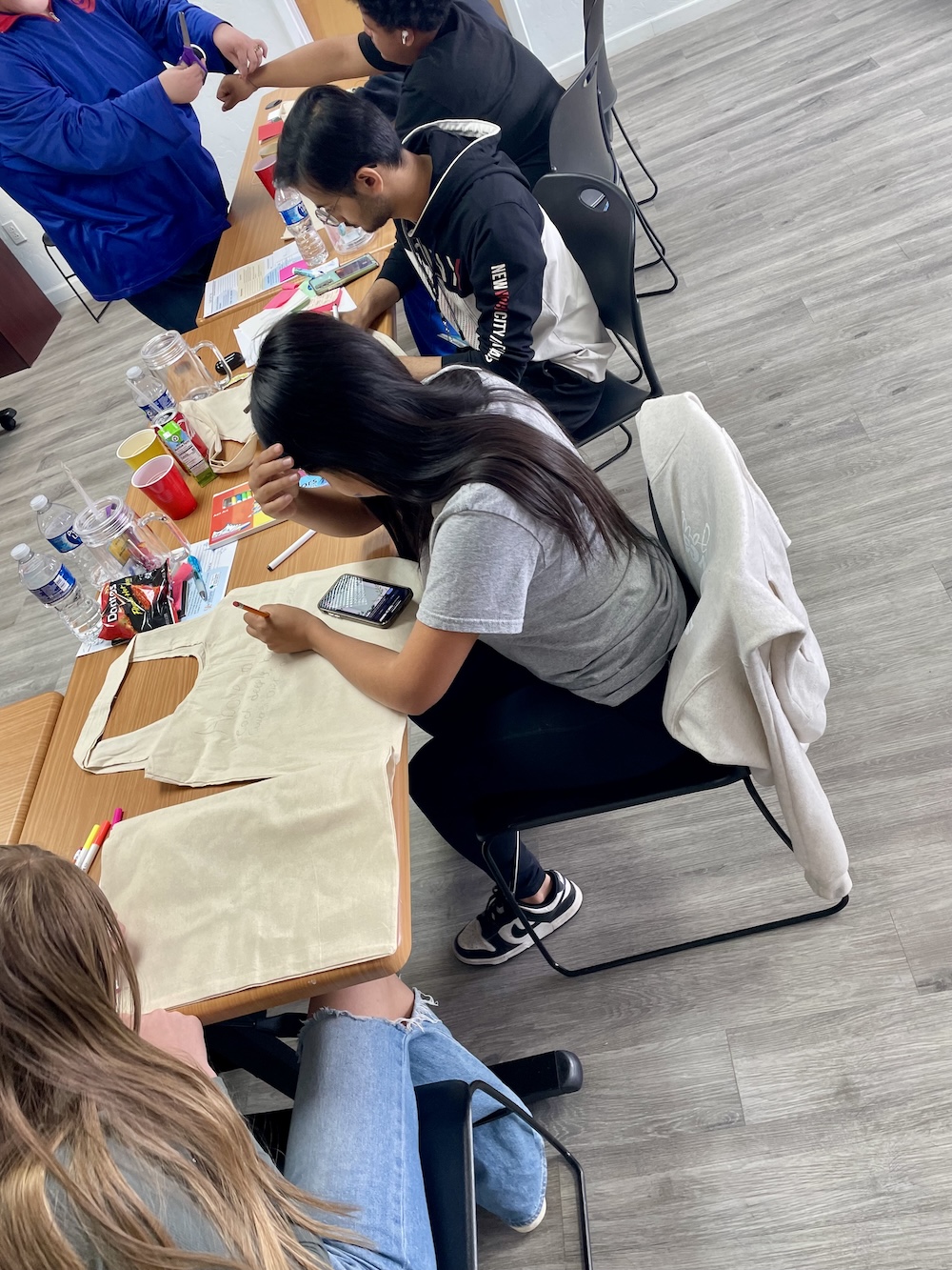 Teens seated at table decorating canvas tote bags in a classroom