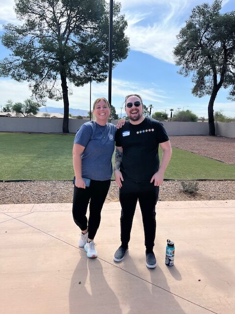 Two smiling adults on a sunny courtyard by turf and trees