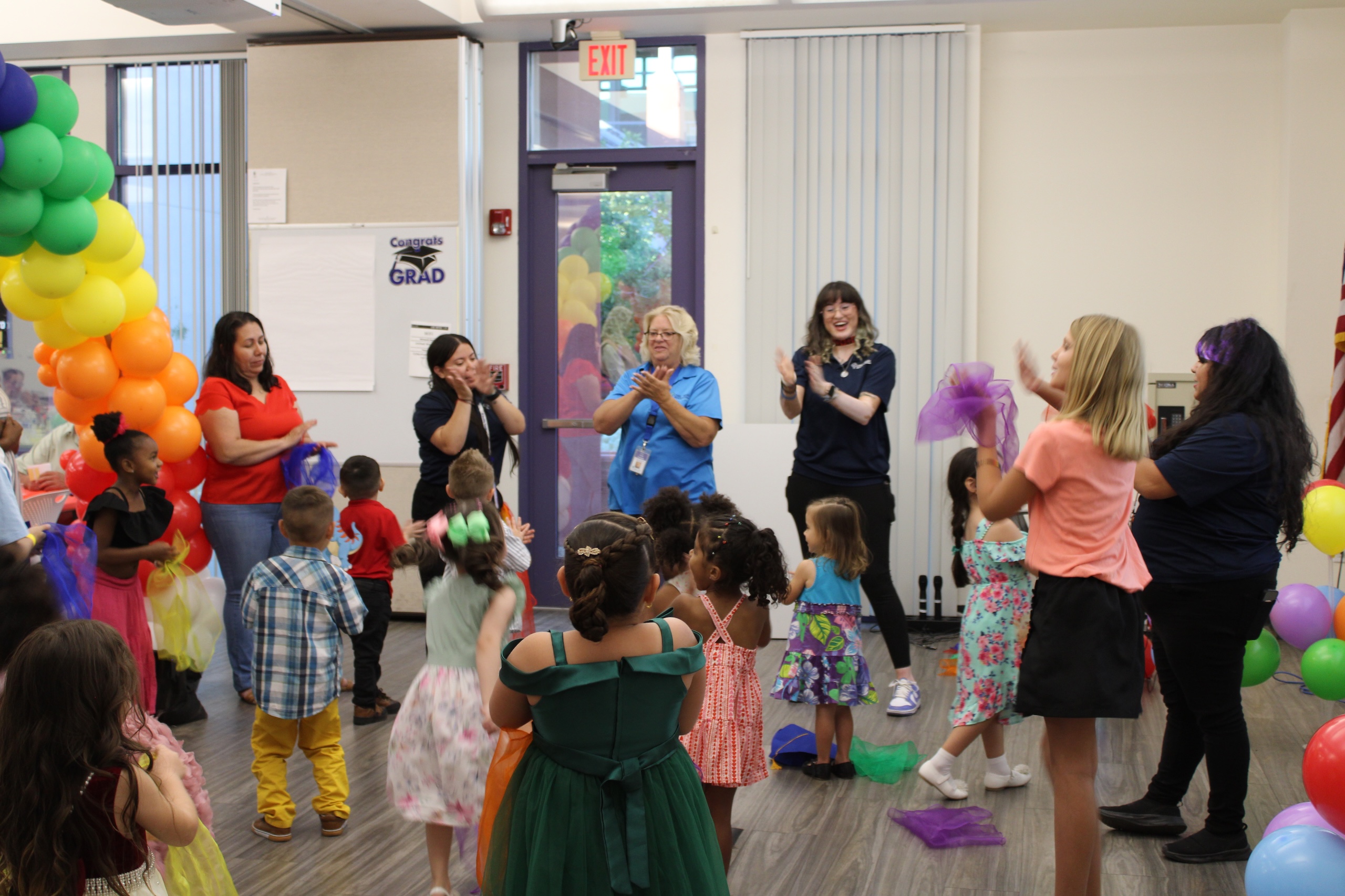 Healthy Families graduation with children and staff clapping and dancing in a community room with rainbow balloon arch