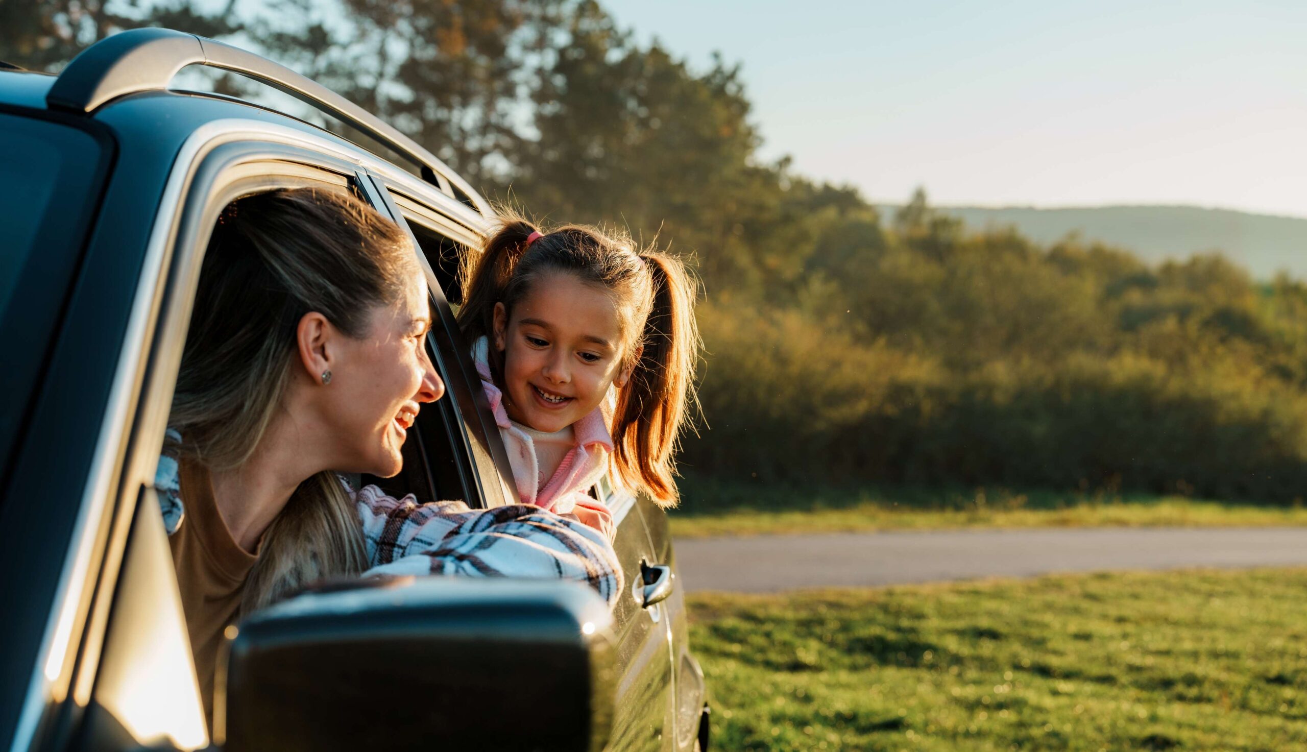 Mother smiling at daughter leaning from car window