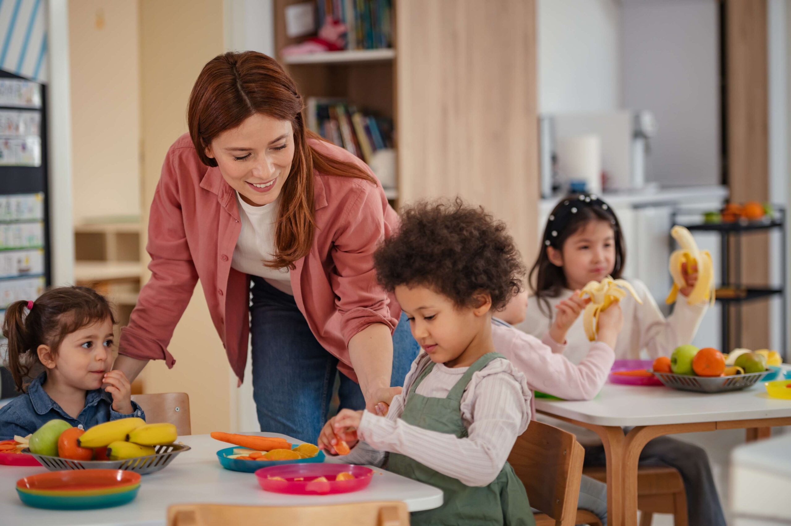 Smiling teacher helps preschool children at a classroom